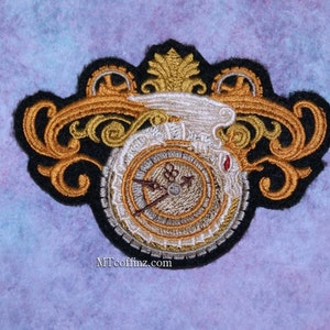 May include: Embroidered patch featuring a gold clock face with Roman numerals and a black and white clock hand. The clock is surrounded by gold and black ornate details and a white wing.