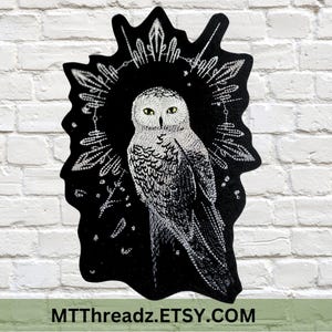 May include: Black embroidered patch featuring a white snowy owl with yellow eyes, surrounded by a circular design of stylised feathers and dots. The patch has a black background and is outlined in white. The text "MTTThreadz.ETSY.COM" is at the bottom of the patch.