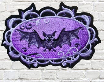 May include: Purple embroidered iron-on patch featuring a black bat in a decorative frame. The bat is flying with its wings spread wide. The frame is made of swirls and vines. The text "MTTThreadz.ETSY.COM" is at the bottom of the image.