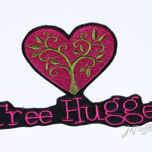 May include: Embroidered patch with a pink heart containing a green tree design and the text "Tree Hugger" in black with pink outlines.