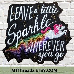 May include: Black embroidered patch with the text "LEAVE a little Sparkle WHEREVER you go". Features a white unicorn with a pink mane and tail, riding a rainbow. Gold diamond accents are scattered around the text and unicorn.