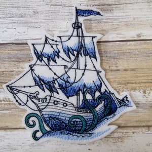 May include: Embroidered patch of a ghostly ship with a blue and white color scheme, being swallowed by a green and blue tentacle. The ship has a tattered sail and is surrounded by blue waves.