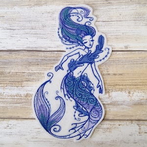 May include: Embroidered patch of a mermaid with blue and purple hair and tail. The mermaid is wearing a seashell bra and has a pearl necklace.