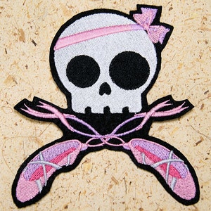 May include: Embroidered patch showing a white skull with a pink headband and bow. Below the skull are crossed pink ballet slippers with ribbons. The patch has a black border and is on a textured background.