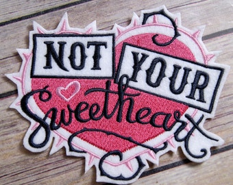 May include: A pink and white heart-shaped embroidered patch with black stitching. The patch says "Not Your Sweetheart" with a small heart in the center.