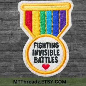 May include: Embroidered patch with a rainbow ribbon and a gold circle with the text "Fighting Invisible Battles" and a small red heart.