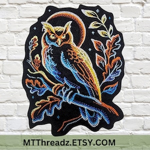 May include: A colorful embroidered patch featuring an owl perched on a branch, set against a black background. The owl is depicted with blue, orange, and yellow thread, with a crescent moon and foliage. The text "MTThreadz.ETSY.COM" is at the bottom.