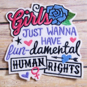 May include: Embroidered patch with the words "Girls Just Wanna Have Fun-damental Human Rights." The patch features a pink cursive "Girls" and a blue rose. Other elements include hearts, stars, and a female symbol.