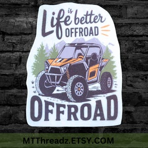 May include: A white sticker with the text "Life is better OFFROAD" above an orange and black off-road vehicle illustration. The word "OFFROAD" is also printed in large letters at the bottom. The sticker has a mountain and tree background.