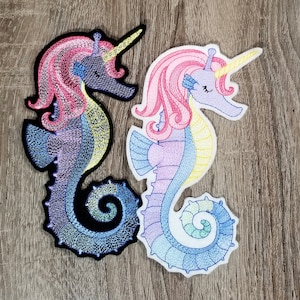 May include: Two embroidered seahorse patches with unicorn horns. One is purple with pink and yellow accents, the other is black with pink and yellow accents.