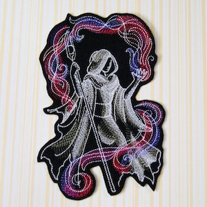 May include: Embroidered iron-on patch featuring a white figure in a hooded robe holding a staff, surrounded by swirling red and blue flames.