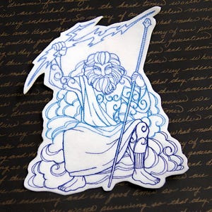 May include: Embroidered patch of Zeus, the Greek god of the sky and thunder, holding a lightning bolt and sitting on a cloud. The patch is white with blue embroidery.