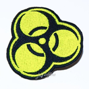 May include: A yellow biohazard symbol patch with black outlines. The patch is made of embroidered fabric.