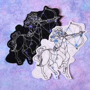 May include: Two embroidered patches featuring the Sagittarius zodiac sign. One patch is black with white and blue stitching, the other is white with black and blue stitching. The patches depict a centaur archer with constellation details.