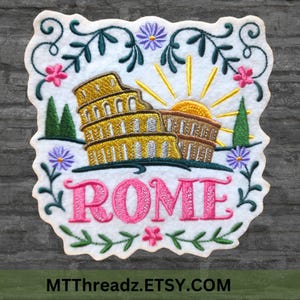 May include: Embroidered patch with a white background featuring a colorful illustration of the Colosseum in Rome, Italy. The patch also includes a yellow sun, green trees, and pink flowers. The word "ROME" is embroidered in pink letters below the Colosseum.