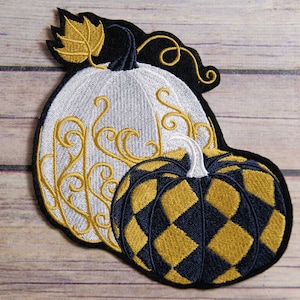 May include: Two embroidered pumpkins, one white with gold swirls and one black and gold with a checkered pattern.