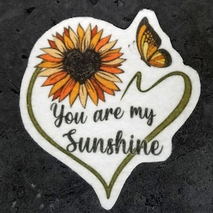 May include: A white heart-shaped sticker with a sunflower and a butterfly. The text "You are my Sunshine" is written in black cursive.
