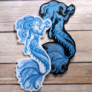 May include: Two embroidered patches of mermaids with blue and white thread on a white background. The mermaid on the left is holding a fish in her hand. The mermaid on the right is black with blue and white thread.