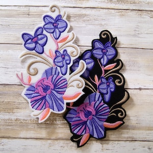May include: Two embroidered iron-on patches featuring purple and pink orchid flowers with gold accents. The patches are on a white and black background.