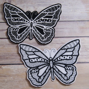 May include: Two black and white embroidered butterfly patches. The butterfly on the left is black with white embroidery. The butterfly on the right is white with black embroidery.