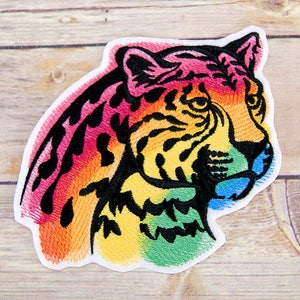 May include: Rainbow colored embroidered iron-on patch of a cheetah's head. The cheetah's fur is black and white with a rainbow gradient.