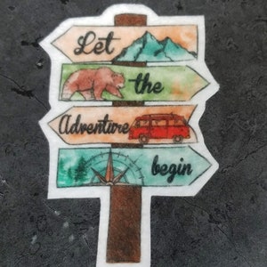 May include: A watercolor illustration of a wooden signpost with four arrows pointing in different directions. The arrows have the words "Let the adventure begin" written on them. The signpost is decorated with a mountain, a bear, a camper van, and a compass.