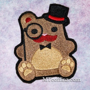 May include: Embroidered patch featuring a brown teddy bear with a black top hat, monocle, and red mustache. The bear has a black bow tie and paw prints. The patch has a black border and the text "MTcoffinz.com".