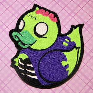 May include: Green and purple embroidered iron-on patch of a cartoon zombie rubber duck with a pink brain and white eyes.