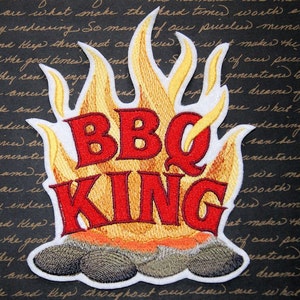 May include: Embroidered patch with a white background and a red and yellow flame design. The text "BBQ KING" is in red letters.