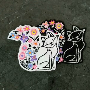 May include: Three embroidered iron-on patches featuring a black cat, a white cat with flowers, and a white cat with flowers and a floral design.