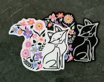 May include: Three embroidered iron-on patches featuring a black cat, a white cat with flowers, and a white cat with flowers and a floral design.