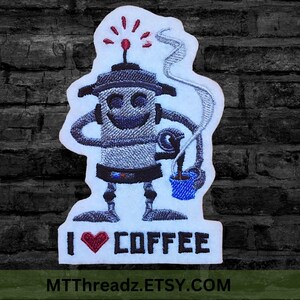 May include: Embroidered iron-on patch featuring a cartoon robot holding a cup of coffee with steam rising from the cup. The robot has a happy face and is wearing a red light on its head. The text "I ♥ COFFEE" is below the robot. The text "MTTThreadz.ETSY.COM" is at the bottom of the patch.