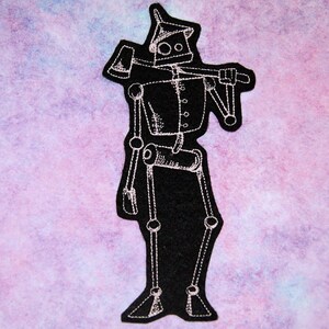 May include: A white outline of a robot with an axe on its shoulder, embroidered on a black felt patch.