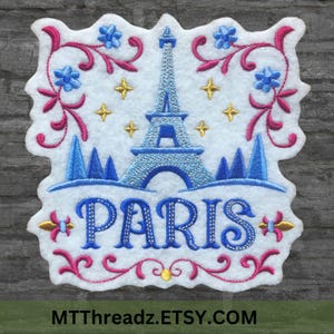 May include: Embroidered patch featuring a blue and white Eiffel Tower with a pink and blue floral design and the word "PARIS" in blue with gold accents. The patch is on a white background.