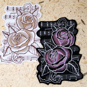 May include: Two embroidered patches featuring roses on a musical note background. One patch is white with brown roses and the other is black with purple roses.