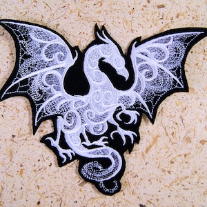 May include: A black and white embroidered patch depicting a dragon with intricate details. The dragon is in flight with its wings outstretched. The design is reminiscent of a Celtic knot.