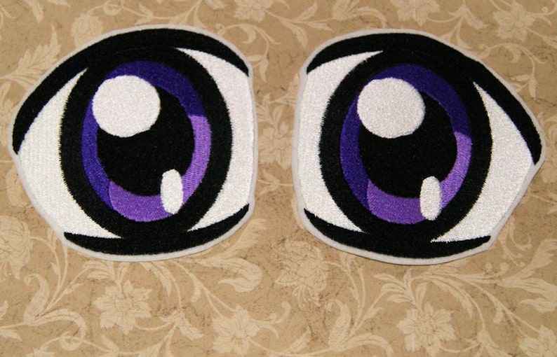 May include: Two white fabric patches with embroidered anime-style eyes. The eyes are black with purple irises and white pupils.