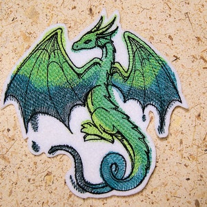 Peut inclure: Dragon vert brodé avec des ailes déployées, sur un fond de feutre blanc.