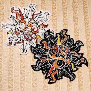 May include: Two embroidered sun patches, one white with orange and yellow details, the other black with orange and yellow details.