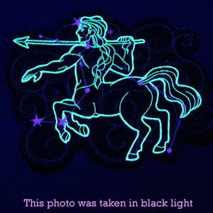 May include: A glow-in-the-dark embroidered patch depicting the constellation Sagittarius. The patch features a centaur holding a bow and arrow, with stars connecting the figure's outline. The patch is designed to be sewn onto fabric.