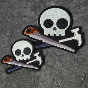 May include: Two black and white embroidered patches with a skull and crossbones design. The crossbones are a saw and a hammer.