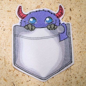 May include: Embroidered patch of a purple monster with red horns peeking out of a gray pocket. The monster has large blue eyes and a toothy grin.