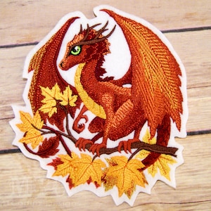 May include: Embroidered patch of a red dragon with orange wings perched on a branch with fall leaves. The dragon has green eyes and a white background.