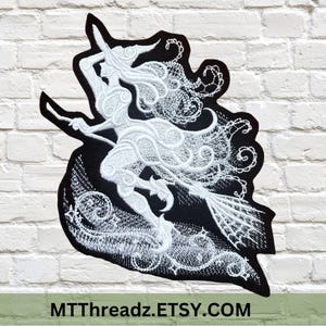 May include: A black and white embroidered patch featuring a witch riding a broom. The witch is depicted in white thread with flowing hair and a pointed hat. The patch has a detailed design with intricate patterns and the text MTThreadz.ETSY.COM.