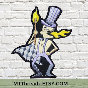 May include: Embroidered iron-on patch featuring a cartoon character with a purple top hat, a checkered cape, and a flaming torch. The character is wearing a purple and white outfit and has a mustache. The text "MTTThreadz.ETSY.COM" is at the bottom of the patch.