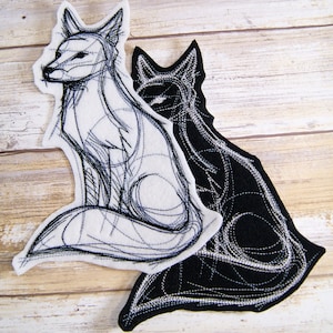 May include: Two embroidered fox patches, one white and one black, with a line art design. The white fox is sitting with its tail curled around its legs. The black fox is sitting with its tail curled around its body. Both foxes are facing to the right.