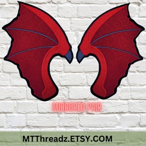 May include: A pair of red dragon wings with blue accents. The wings are mirrored and are made of felt. The text "MIRRORED PAIR" is written below the wings. The text "MTTThreadz.ETSY.COM" is written below the text "MIRRORED PAIR".