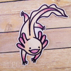 May include: An embroidered patch of a pink and white axolotl with a purple outline. The axolotl is smiling and has a long tail.