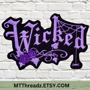 May include: Black embroidered patch with the word "Wicked" in purple gothic lettering. The patch features a spider web, a spider, and floral accents. The patch is against a white brick wall.