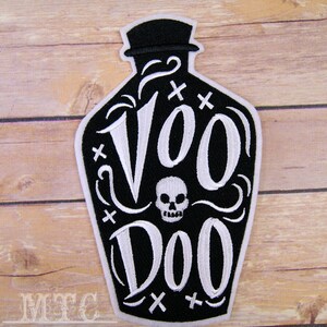 May include: Black and white embroidered patch of a bottle with a skull and the text "Voodoo" on it.